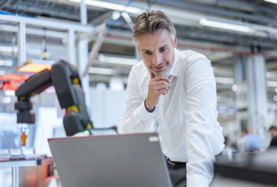 Confident businessman in a modern factory hall using laptop