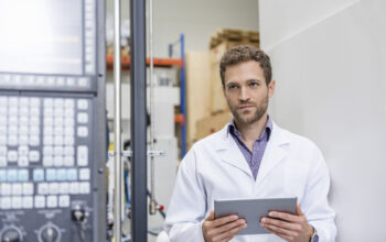 Employee checking manufacturing machines in high tech company, using digital tablet