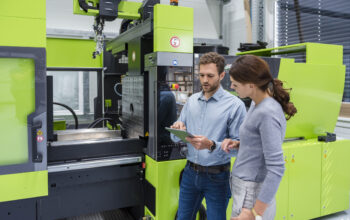 Colleagues in high tech company controlling manufacturing machines, using digital tablet